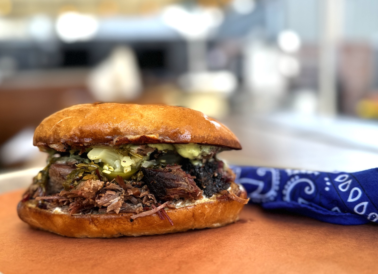 A chopped brisket sandwich on a roll with a blue bandana napkin