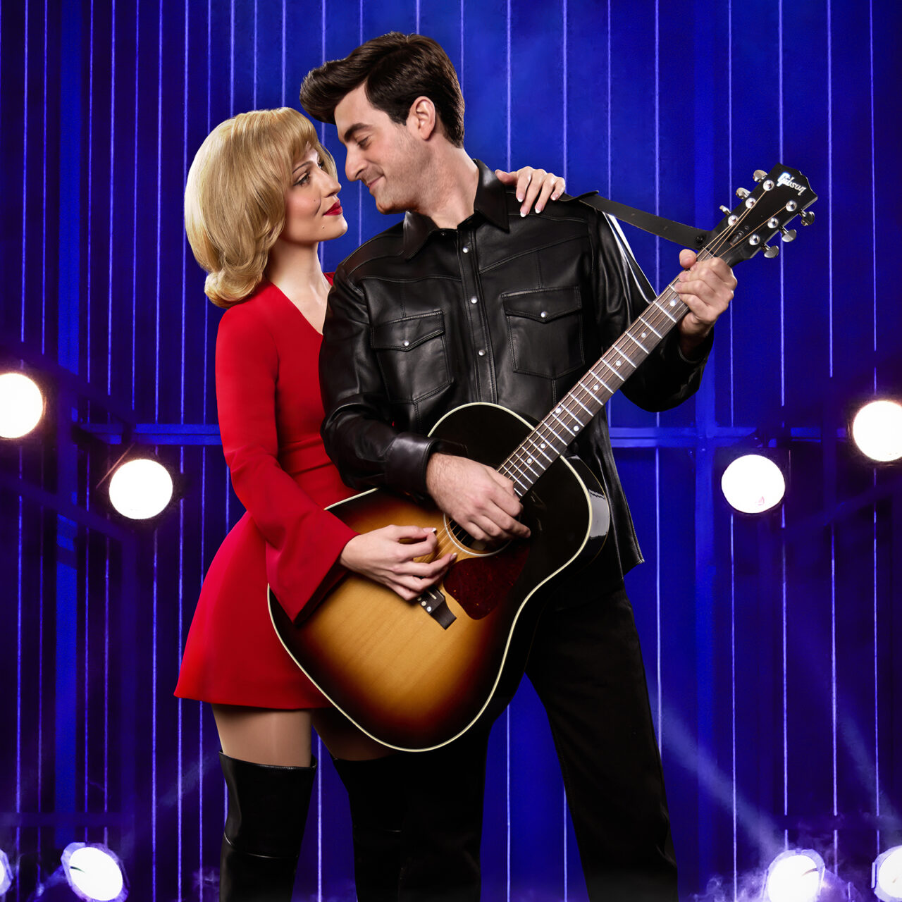A girl in a red dress and a man in black leather with a guitar in a production of “A Beautiful Noise”