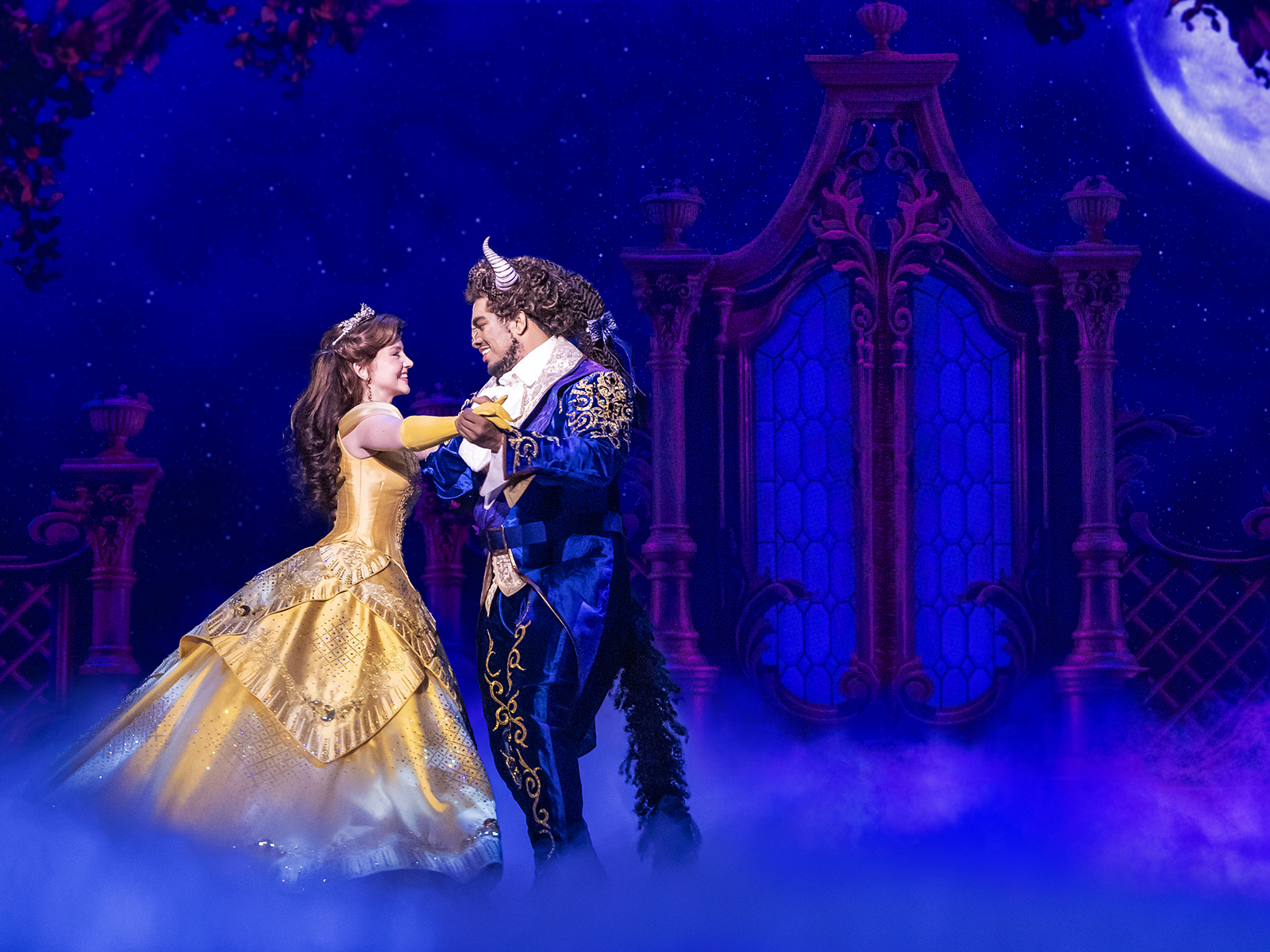 A girl in a yellow dress dances with a beast in a blue suit in a production of “Disney’s Beauty and the Beast”