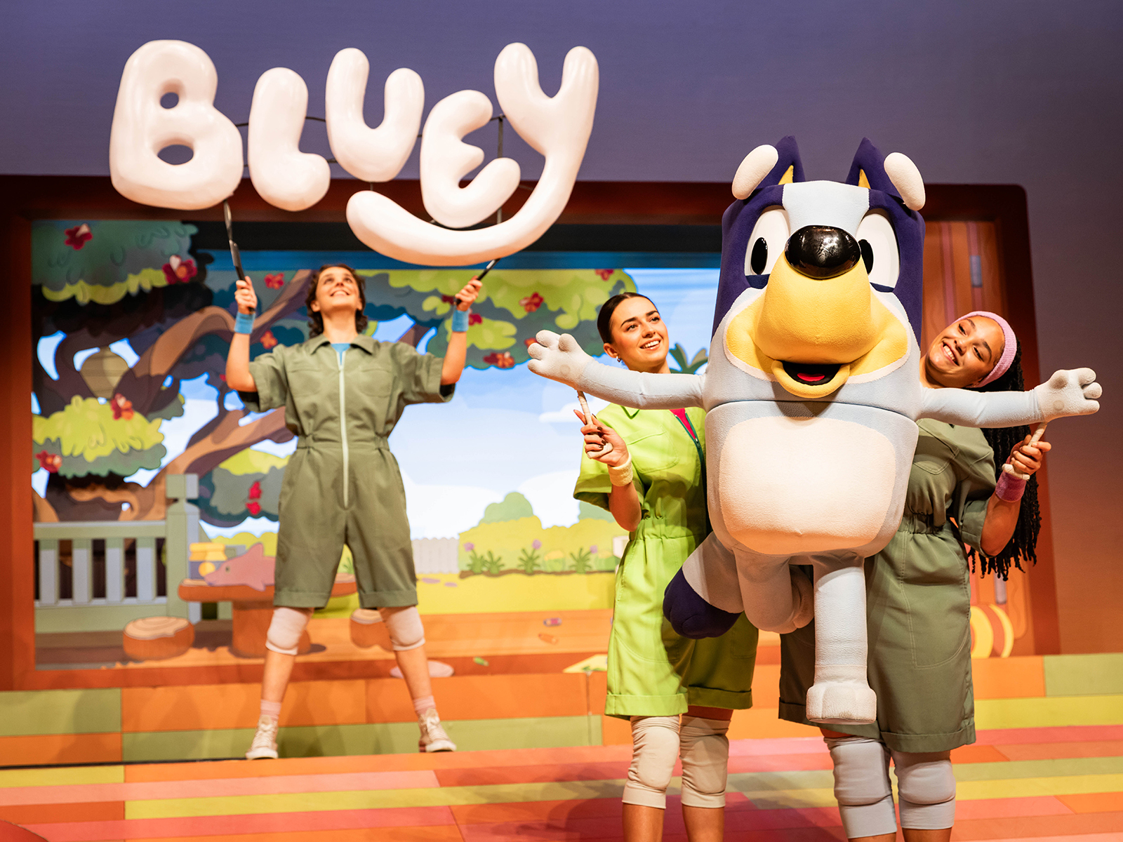 A blue heeler prop is held by stage actors in a production of “Bluey’s Big Play”